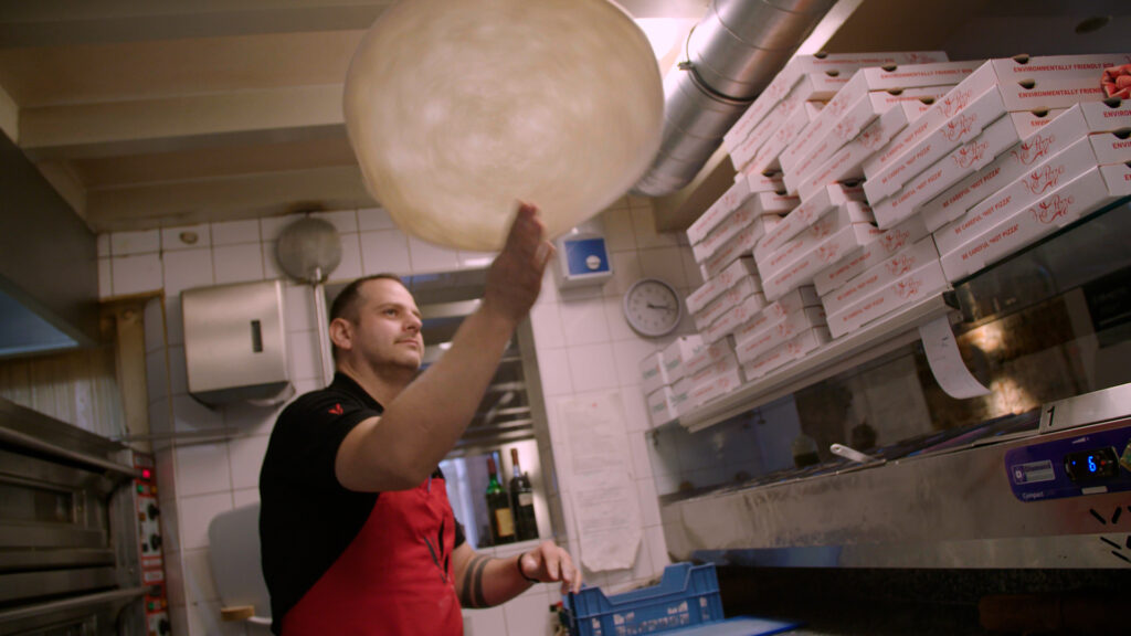 Eigenaar van Piccola Italia bakt een pizza.